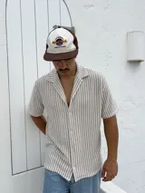 Camisa tejida a rayas verticales color beige y blanco, de corte recto, manga corta y cuello cubano.