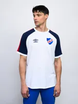 Remera de algodón azul con mangas ranglan azul marino y detalles en blanco en cuello y puños. Incluye logo de Umbro y escudo del Club Nacional de Football en el frente.