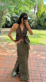 Falda larga color verde oliva con múltiples capas de flecos largos, creando un efecto texturizado. La falda tiene un tajo lateral.