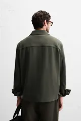 Sobrecamisa color beige de corte relaxed fit, con cuello solapa, manga larga con puños abotonados, bolsillos de plastrón con solapa en el pecho y bolsillos de vivo en la cadera. Cierre frontal con botones.