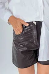 Short de cuero negro con cintura alta, cierre frontal con botón y bolsillos laterales.