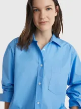 Camisa celeste de popelín de algodón orgánico, corte oversize con hombros caídos, cuello inglés, bolsillo de parche en el pecho y logo bordado en la manga.