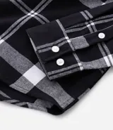 Camisa de franela para hombre con estampado de cuadros en blanco y negro. Tiene cuello inglés, mangas largas, bolsillos en el pecho y abotonado delantero.