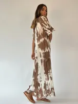 Vestido largo color beige con estampado tie-dye en tonos rosados, corte amplio, mangas cortas con volados y ruedo con flecos.