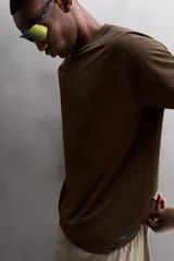 Camiseta deportiva marrón con estructura perforada, cuello redondo, manga corta y logo estampado.