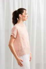 Blusa de lino color rosado, de corte holgado, con cuello redondo y detalle de encaje en ruedo y mangas.