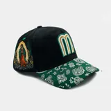 Gorra de béisbol negra con visera estampada con diseño paisley verde y blanco. Presenta un bordado de la Virgen de Guadalupe en el panel lateral y una letra 'M' estilizada en el frente con franjas blancas, verdes y doradas.