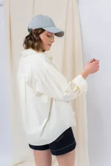 Camisa color crema de algodón liviano, calce oversize, con cuello camisero, cierre abotonado, mangas largas con opción de arremangado y dos bolsillos frontales con solapa.