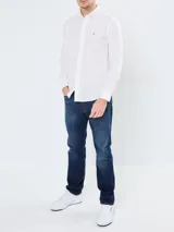 Camisa blanca de popelina de algodón flexible, con cuello abotonado, cierre frontal con botones y puños abotonados. Tiene logo de Tommy Hilfiger bordado en el pecho.