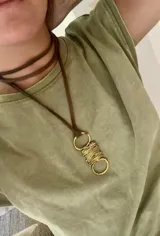 Collar con colgante de bronce dorado con forma geométrica y cordón de cuero marrón.