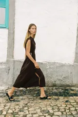 Vestido midi marrón de lino con cuello solapa, escote en pico y sin mangas. Presenta trabillas laterales con cinturón y cierre frontal con botones.