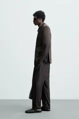 Blazer negro de corte relaxed fit, confeccionado en tejido de algodón con acabado ligeramente encerado. Tiene cuello con solapas de muesca, manga larga con puños abotonados, bolsillo de vivo en el pecho, bolsillos de solapa en la cadera, bolsillo interior, aberturas en la espalda y cierre frontal con botones.