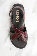 Sandalia marrón con tiras cruzadas de cuero con textura de cocodrilo, suela track color negro y hebilla metálica.