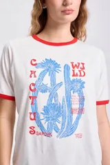 Remera blanca de manga corta con cuello y mangas con ribete rojo. Estampa frontal con diseño de cactus y texto en azul y rojo.