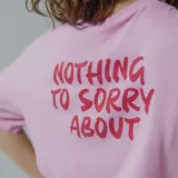 Remera rosada con estampa en el centro de la espalda con la frase "Nothing to sorry about" en color rojo.