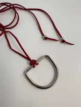 Collar con dije de estribo metálico plateado y cordón de cuero sintético color bordó con terminales plateadas.