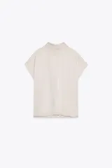 Blusa color crudo de tejido satinado, con cuello subido, manga sisa y cierre en la espalda con lazada y botones.