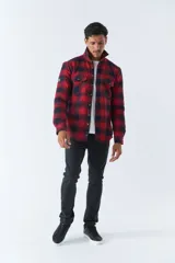 Sobrecamisa de algodón para hombre con interior de corderito, estampado a cuadros en tonos negro, blanco y azul. Tiene cierre de botones, bolsillos tipo cartera y logo en goma. El modelo usa talle M.