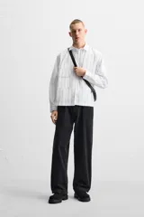 Camisa cropped fit confeccionada en tejido de algodón a rayas verticales negras sobre fondo blanco. Cuello solapa y manga larga acabada en puño con botones. Bolsillos frontales de plastrón con solapa. Cierre frontal de botonadura.