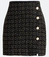 Minifalda negra de tweed con estampado a cuadros en dorado, con tres botones decorativos en el frente y abertura lateral.