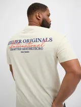 Remera color crema de manga corta con cuello redondo y calce holgado. Estampa en goma ubicada en la espalda con el texto "Atelier Originals Crafted Aesthetics".