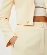 Blazer cropped color amarillo pastel, de crepé con forro de poliéster, cuello solapa, manga larga y cierre frontal con botón en forma de corazón.