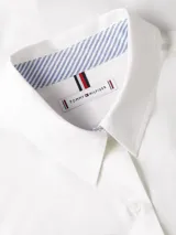 Camisa blanca de manga larga con cuello clásico, bolsillo frontal y logo bordado en el pecho. Presenta detalles distintivos de Tommy Hilfiger en el cuello.