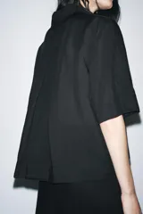 Camisa negra de manga corta confeccionada en hilatura con lyocell y ramio, con cuello solapa, bajo recto y cierre frontal con botones.