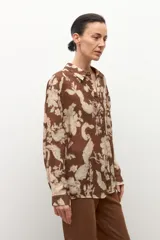 Camisa de manga larga con cuello y botones frontales, confeccionada en tela ligera con estampado floral en tonos marrón chocolate y beige claro.