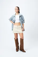 Minifalda color marrón claro, de corte recto con cierre metálico visible al frente y bolsillos decorativos con tachas.