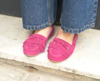 Mocasín de cuero gamuzado color fucsia, con flecos en la capellada y un lazo con herrajes metálicos dorados. Interior forrado en cuero y suela de goma flexible.