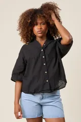 Camisa color beige claro, de corte clásico, con cuello, botones frontales, bolsillo en el pecho y mangas tres cuartos con presilla para sujetar.