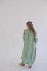 Vestido largo verde con estampado floral en tonos rosados y blancos, mangas 3/4 con ajuste de botón y ruedo irregular.