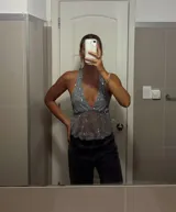 Top halter gris claro, ajustado al cuerpo, con escote pronunciado en V y cubierto de lentejuelas plateadas. El tejido es semitransparente.