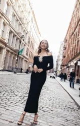 Vestido midi negro de hombros descubiertos confeccionado en punto merian con forro en el cuerpo, presenta bordado de flores 3D en la parte delantera, canesú en el escote con volantes en los laterales y en el centro delantero y una abertura en la espalda.