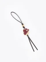 Charm colgante realizado en cuero vacuno color marrón oscuro, con dije central de dragón en relieve color rojo oscuro sobre base metálica dorada. Incluye una correa de cuero para sujetar y flecos decorativos en la parte inferior.