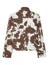 Chaqueta de jean con estampado animal print de vaca en tonos marrones y blancos, corte recto, cuello camisero y cierre frontal con botones.