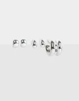 Set de tres pares de aros plateados con diferentes diseños: un par de aros tipo botón con forma irregular, un par de aros colgantes con forma de lágrima y un par de aros tipo argolla gruesa.
