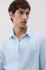 Camisa celeste de lino y algodón, corte regular, manga larga, cuello inglés, bolsillo en el pecho y cierre con botones.