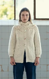 Cardigan tejido a crochet en lana merino color crudo, con volados dobles en hombros y cuello, canesú con tejido abierto y ajuste frontal con cuatro botones de guampa tallados a mano.