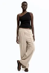 Pantalón de corte holgado color beige, confeccionado en sarga de mezcla de lyocell. Modelo de tiro alto con cintura fruncida, cierre decorativo y bolsillos laterales discretos. Piernas rectas con pliegues cosidos adelante y raya planchada atrás.