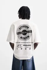 Camiseta blanca de corte relajado, cuello redondo y manga corta. Presenta un estampado de gráficos y textos combinados a contraste en la parte delantera y trasera.