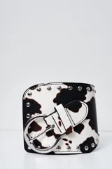 Cinto faja ancho con estampado animal print de vaca en blanco y negro, con hebilla metálica plateada y tachas decorativas.