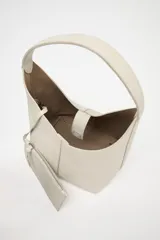 Bolso tipo saca de cuero color gris claro con textura granulada. Tiene asa de hombro y cierre con imán. Incluye cartera interior extraíble con bolsillo.