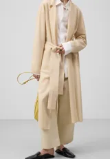 Chaqueta larga color beige de punto doble frontura de galga fina, con solapa, manga larga, bolsillos delanteros y cinturón.