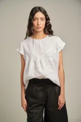 Blusa blanca de lino con cuello redondo, mangas cortas y canesú con alforzas en el frente.