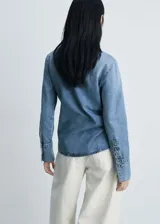 Camisa de jean celeste con cuello camisero y lazo al cuello, de manga larga con puños abotonados y corte recto.