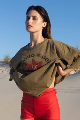 Remera verde militar de corte amplio con estampa en el frente con texto en español y siluetas rojas.
