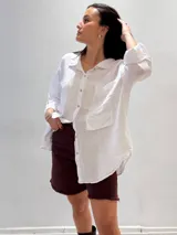 Camisa oversize rosada de lino, con cuello clásico, cierre frontal con botones, dos bolsillos de parche en el pecho y mangas largas con puños abotonados.