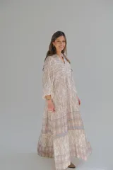 Vestido largo color beige con estampado abstracto en tonos marrones y azules. Tiene cuello mao, mangas largas abullonadas con puños elásticos y falda escalonada.